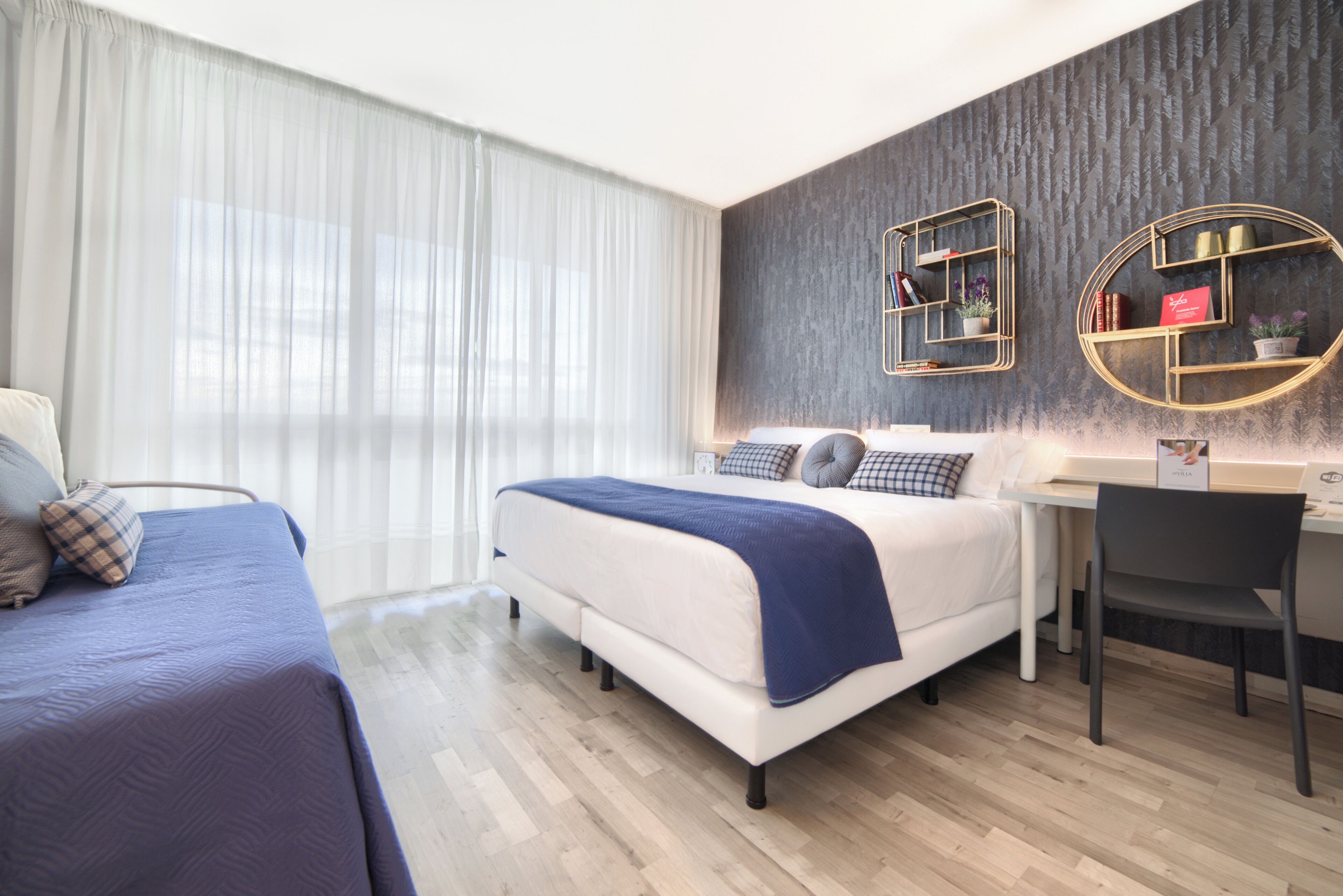 A modern bedroom with a large bed, a smaller bed, a desk, and two decorative shelves.