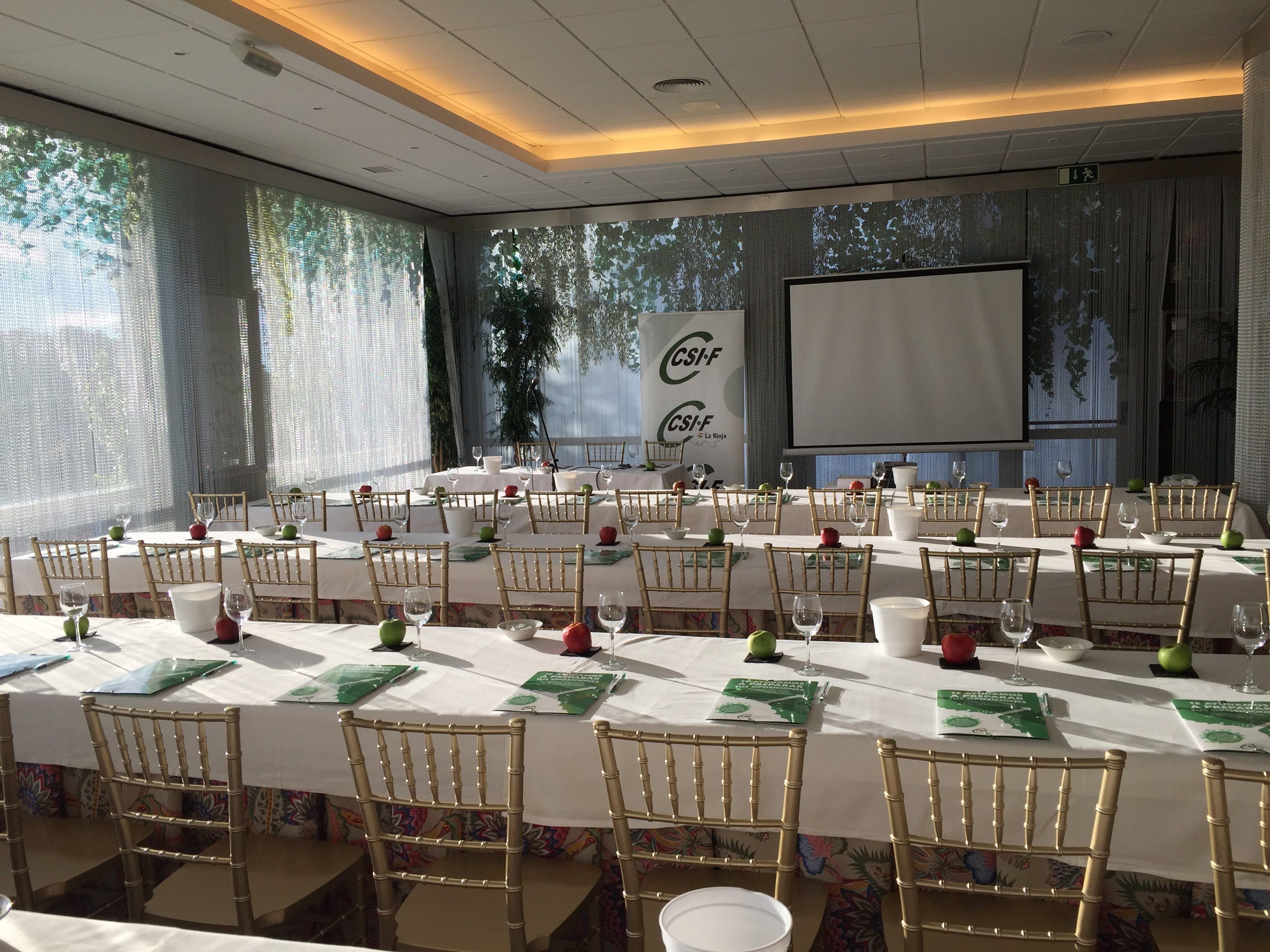 Uma sala de conferências com mesas compridas, cadeiras e uma tela grande.