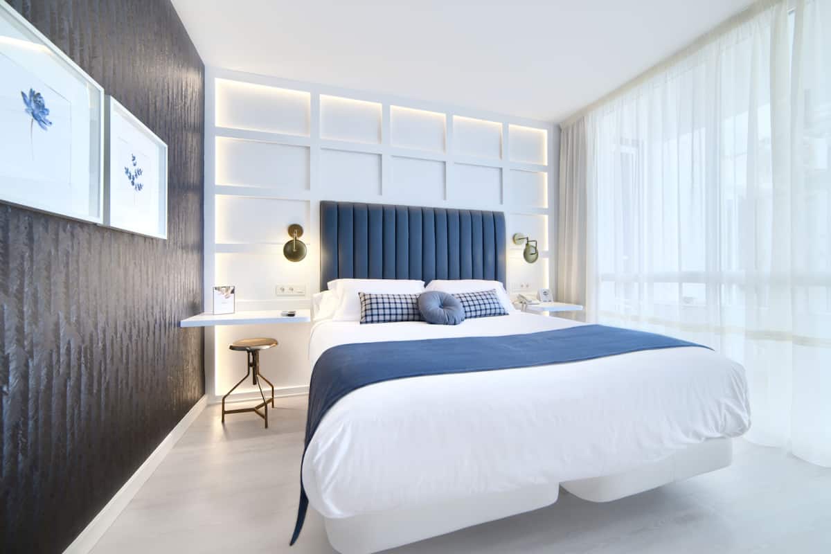 A modern bedroom with a large bed, a bedside table, a nightstand, and a wall-mounted light fixture.