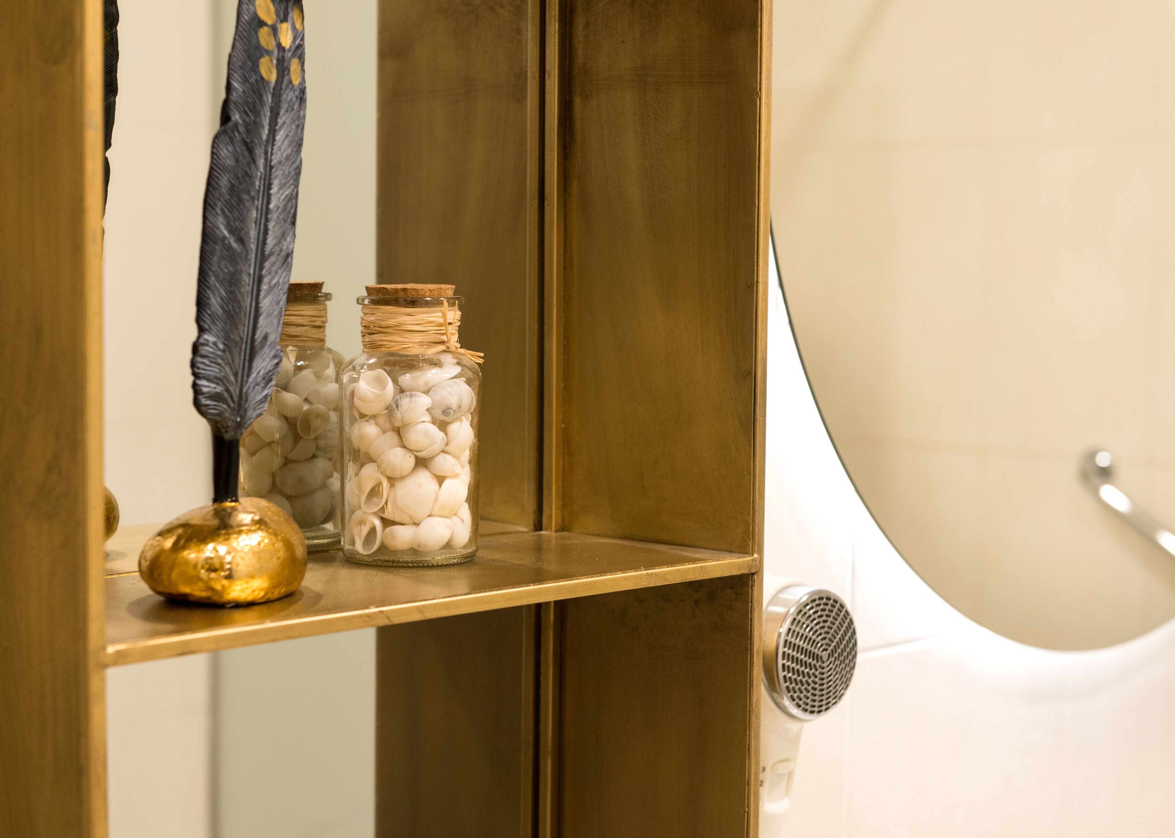 A shelf with decorative jars containing seashells and a feather.
