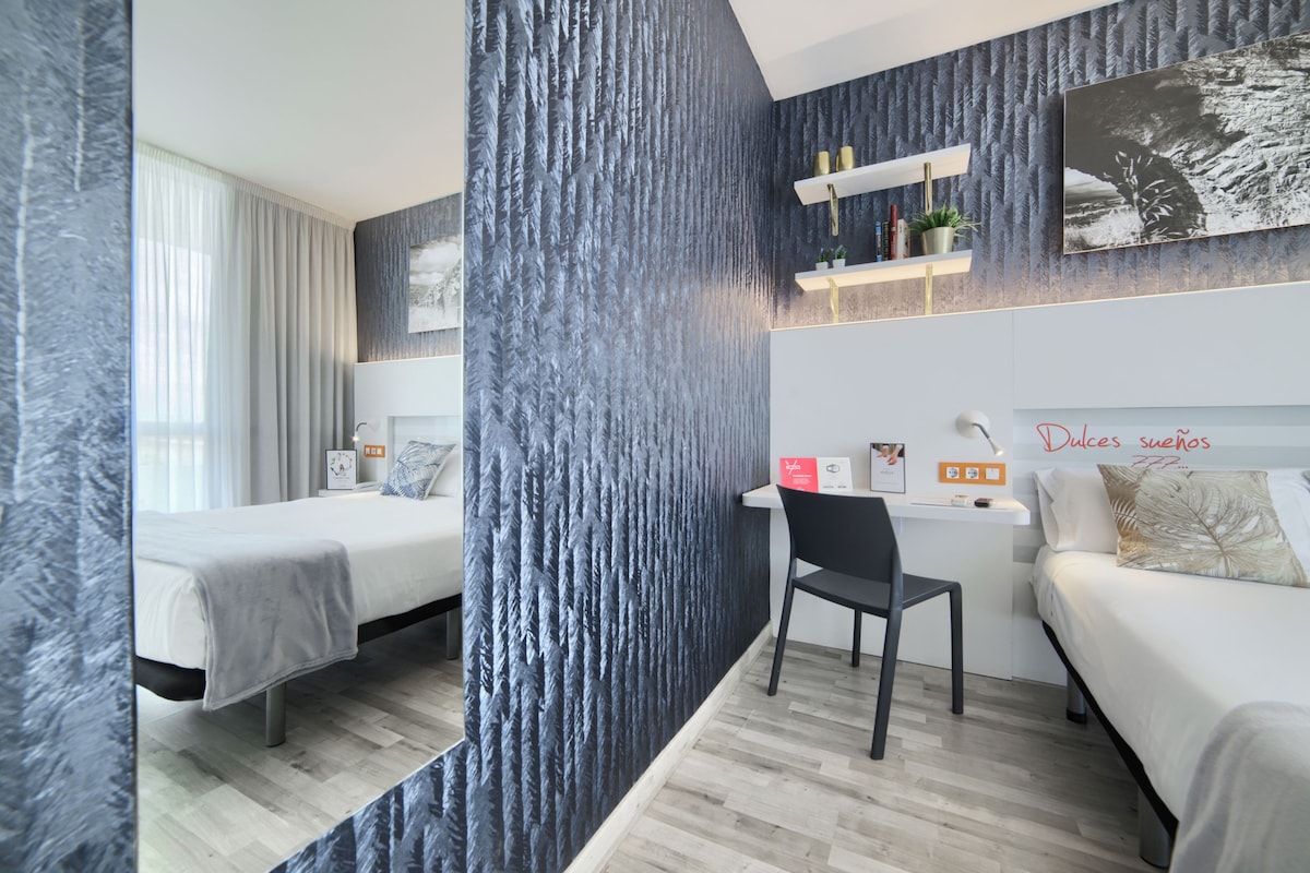 Une chambre d’hôtel moderne équipée de deux lits, d’un bureau et d’une chaise.