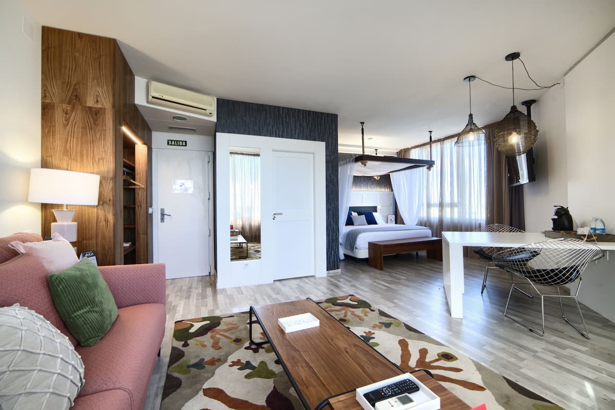 A modern hotel room with a sofa, a coffee table, a bed, a desk, and a TV.