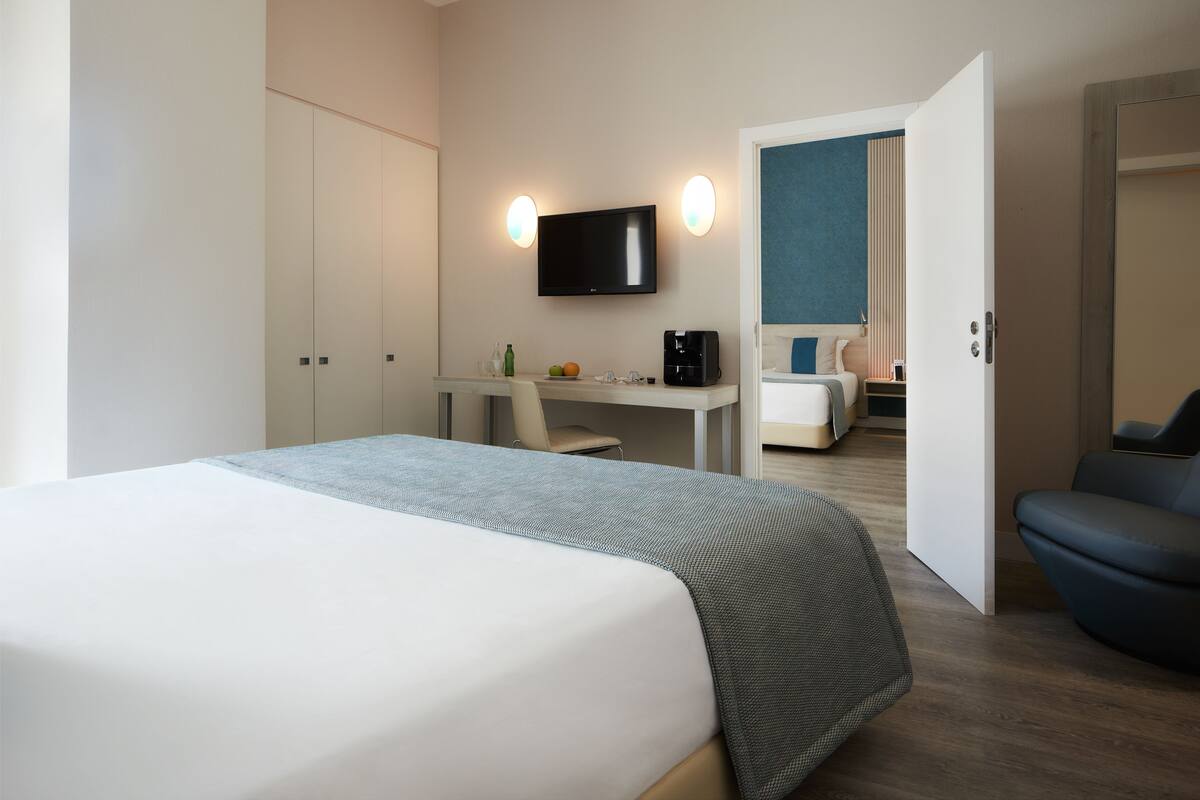 Habitación de hotel con cama, escritorio, silla, televisión y baño visible a través de una puerta abierta.