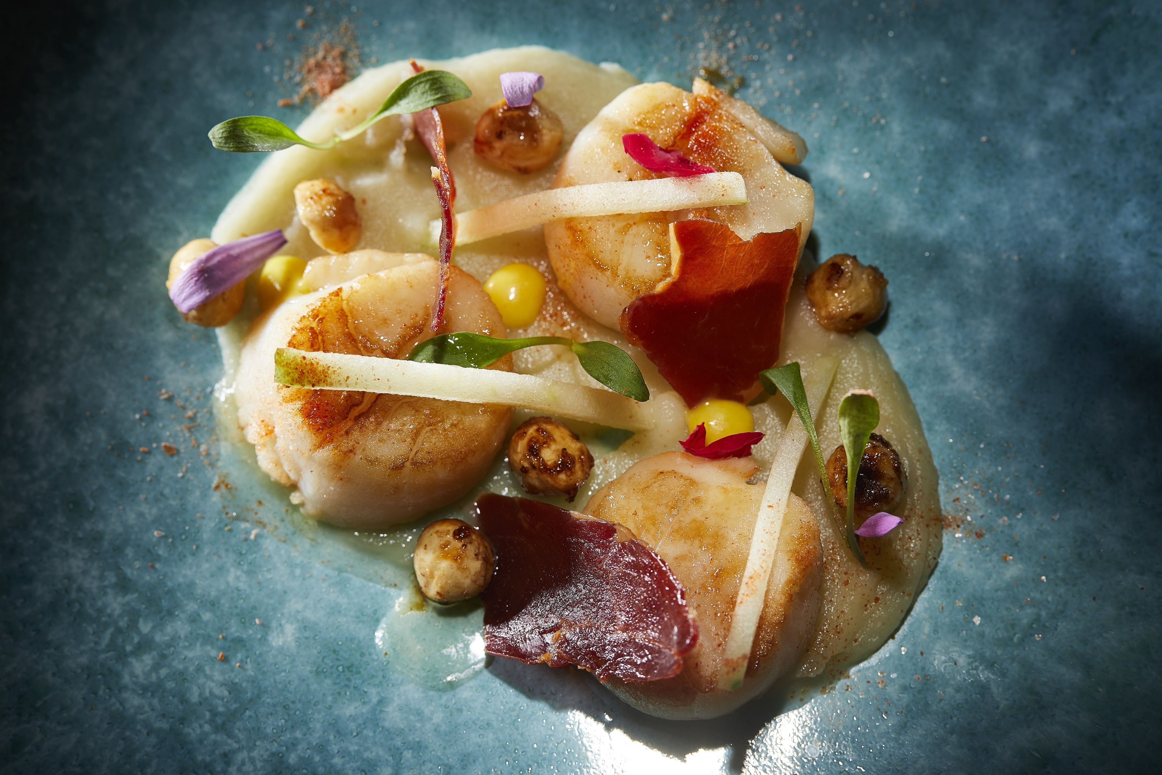 A dish with scallops, corn, and garnishes on a blue plate.