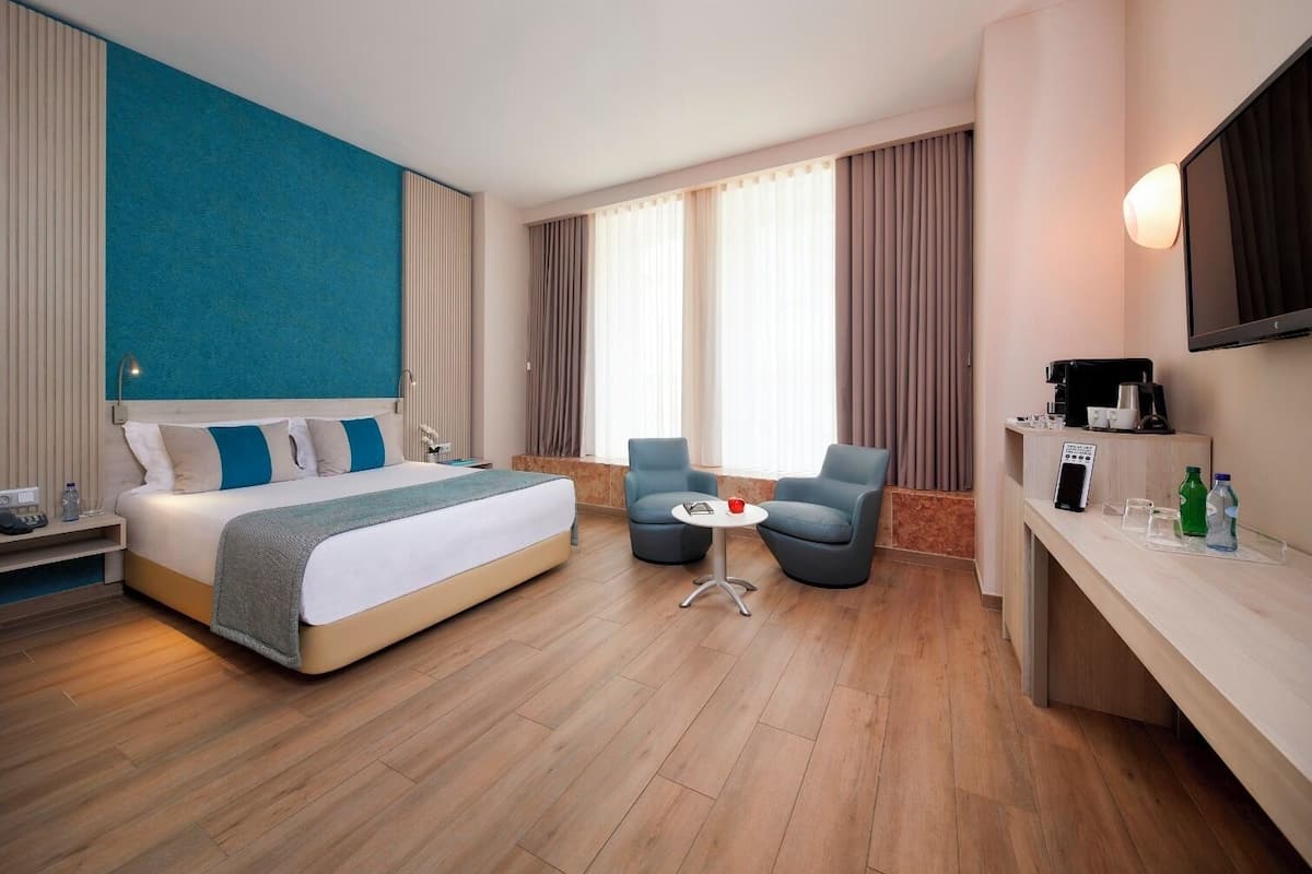 Habitación de hotel con una cama grande, dos sillones, una mesita, televisor y un minibar.