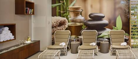 A spa room with wicker chairs, a wooden shelf with books, and a wall mural of natural elements.