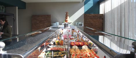 Un bufé con una variedad de alimentos, como ensaladas, carnes y postres, expuestos en una vitrina de vidrio.