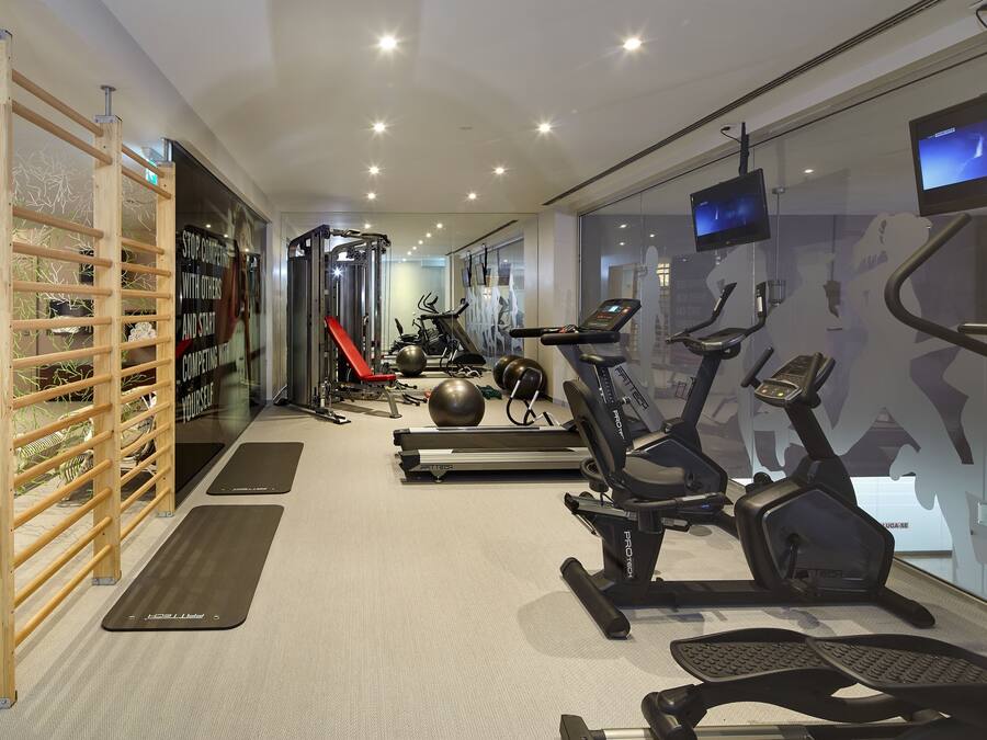 Une salle de sport moderne équipée de tapis de course, de vélos elliptiques et d’un espace dédié à la musculation.