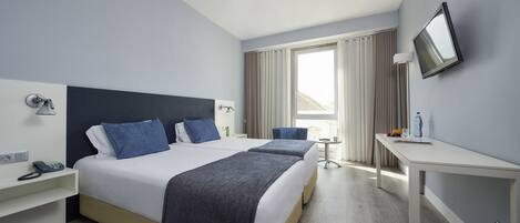 A hotel room with a large bed, a desk, a chair, a TV, and a window with curtains.