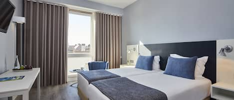 A hotel room with two beds, a desk, a chair, a TV, and a window with curtains.