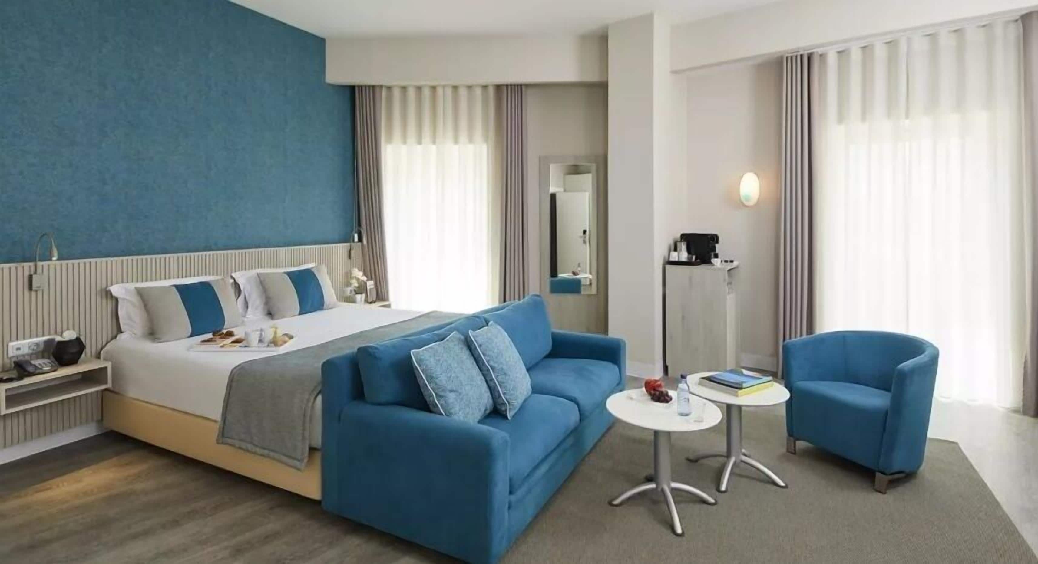 A hotel room with a bed, a blue sofa, a small round table, and a chair.