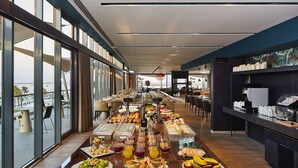 Un buffet proposant une variété de plats et de boissons, un coin café et une vue sur l’extérieur grâce à de grandes fenêtres.
