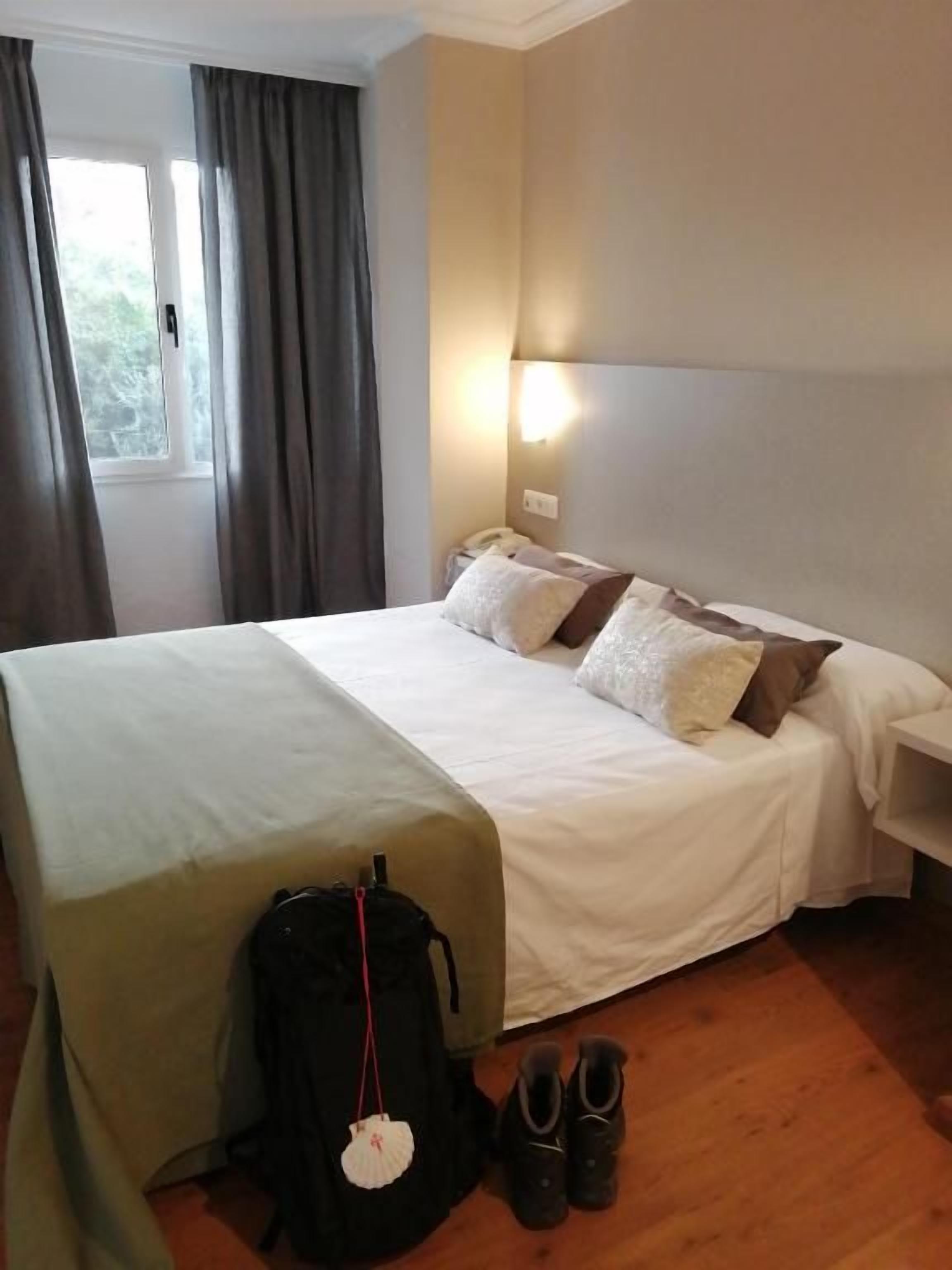 A hotel room with a bed, bedside table, lamp, and a window with curtains.