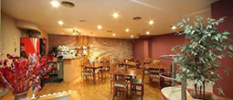 A restaurant with wooden flooring, multiple tables and chairs, a bar area, and a stone wall.