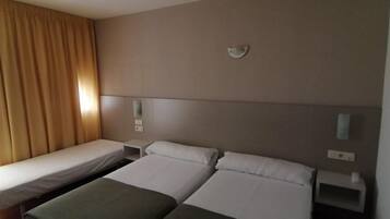 Habitación de hotel con dos camas individuales, una mesita de noche, una lámpara de pared y una ventana con cortinas.