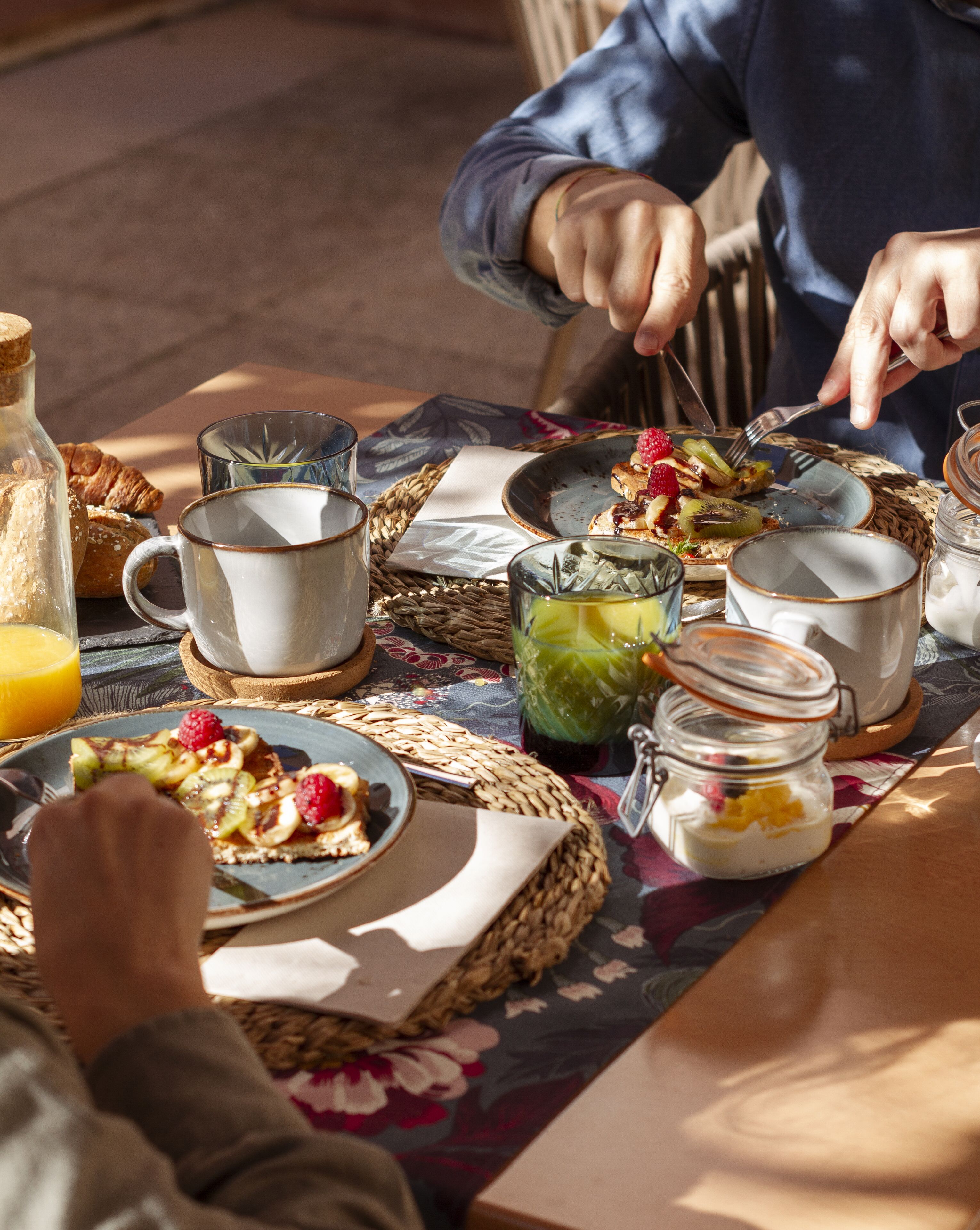 Una mesa para dos lista para el desayuno, con croissants, fruta y un vaso de jugo.