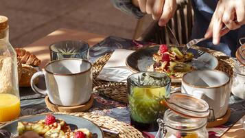 Una mesa para dos lista para el desayuno, con croissants, fruta y un vaso de jugo.