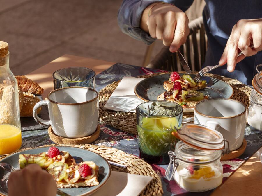 Una mesa para dos lista para el desayuno, con croissants, fruta y un vaso de jugo.
