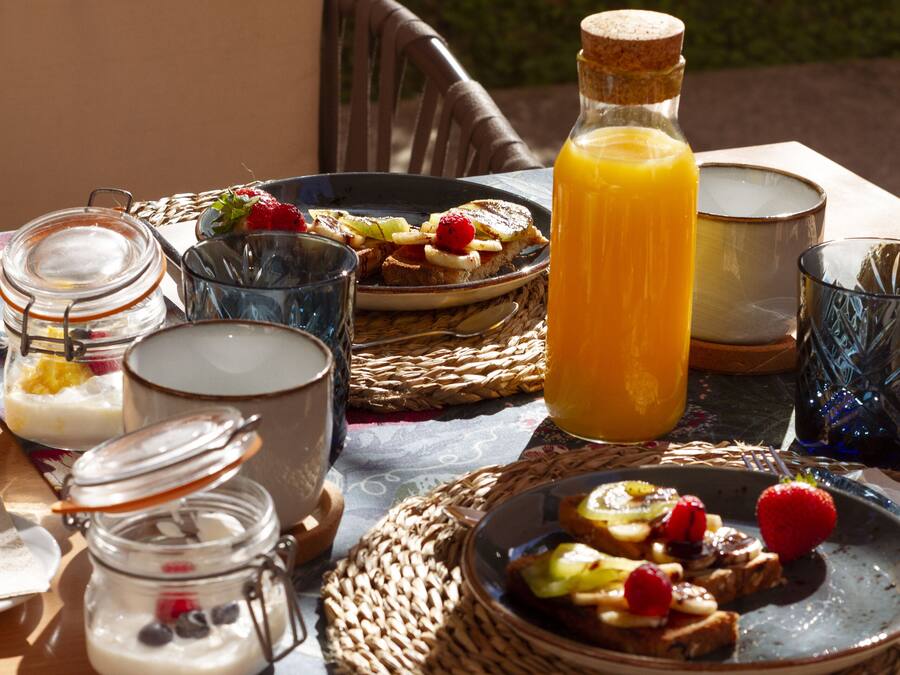 Ein Frühstückstisch mit Rattangeflecht, einer Orangensaftflasche und verschiedenen Frühstücksleckereien.