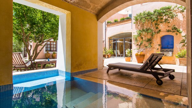 An indoor swimming pool with a sun lounger, a tiled floor, and a view of the outside. -  Hotel Can Moragues (Arta)
