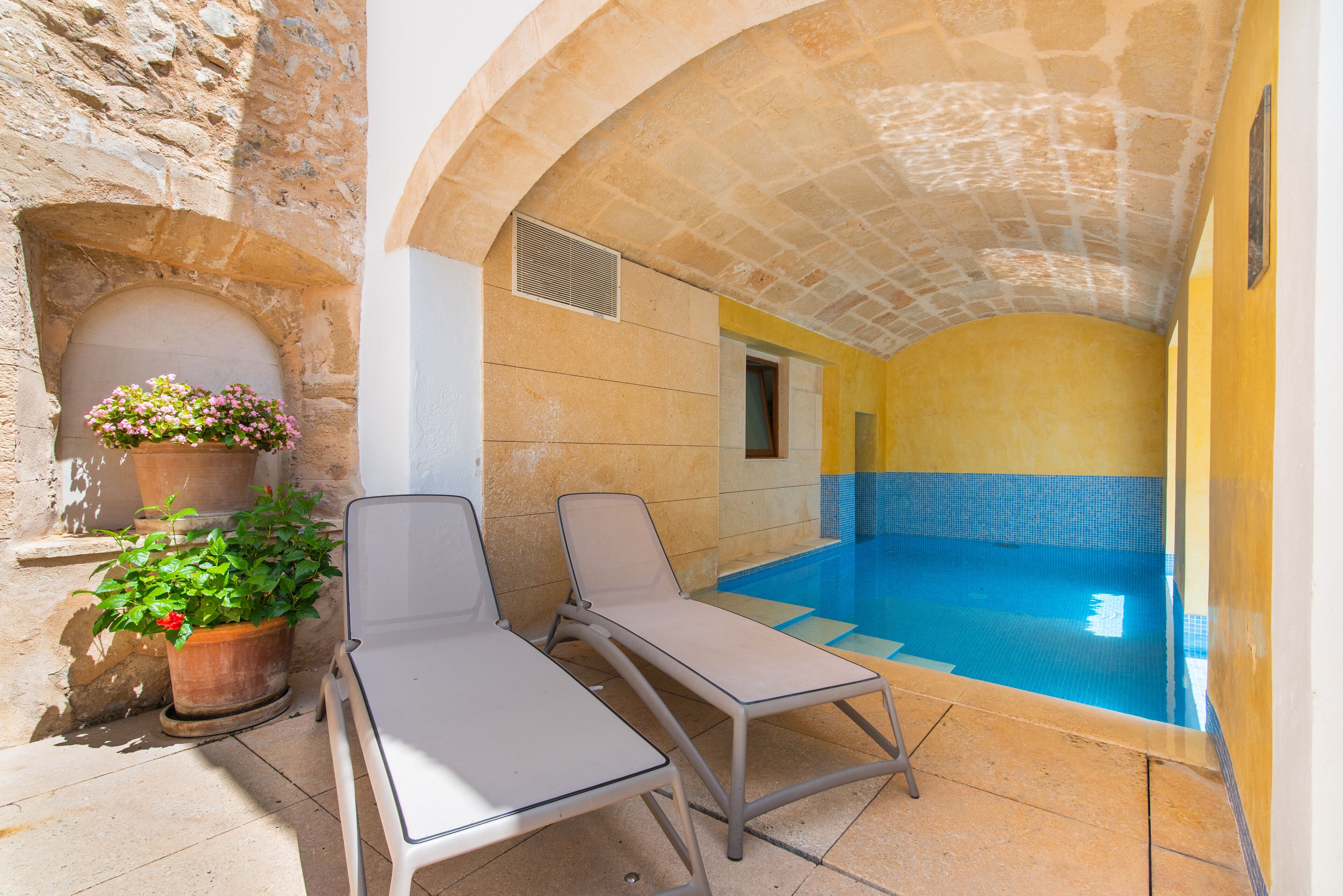 A pool area with two lounge chairs, a potted plant, and a stone wall.