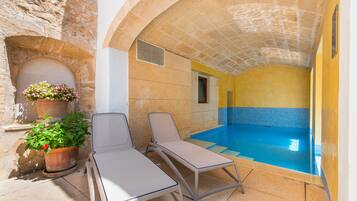 A pool area with two lounge chairs, a potted plant, and a stone wall.