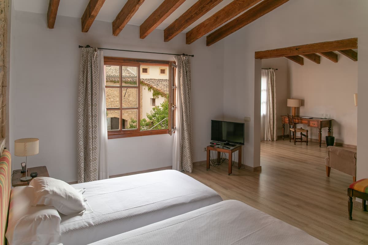 Un dormitorio con dos camas, televisión, escritorio y ventana con cortinas.
