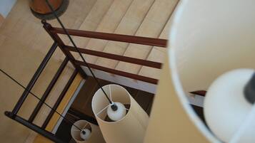 A staircase with a wooden handrail, a potted plant, and two hanging lamps.
