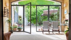 An open glass door leading to a patio with two striped chairs, a table, and potted plants. -  Hotel Can Moragues (Arta)