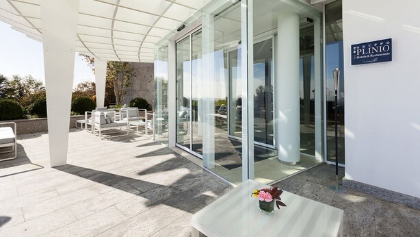 A modern hotel entrance with glass doors, outdoor seating, and a clear view of the surrounding area. - Albavilla Hotel & Co. (Albavilla)