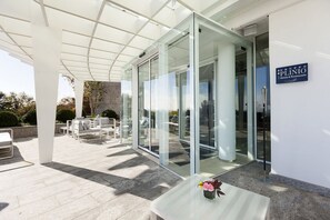 A modern hotel entrance with glass doors, outdoor seating, and a clear view of the surrounding area.