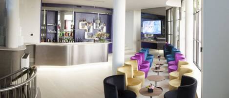 Un hall d’entrée spacieux avec un bar, des sièges aux couleurs vives et un grand écran.