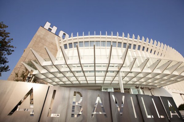 A modern building with a distinctive curved roof and the letters "ALBAVILLA" prominently displayed in the foreground.