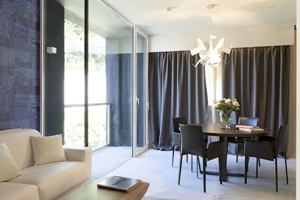 Una sala de estar moderna con un sofá, una mesa de comedor con sillas, una computadora portátil y un florero con flores.