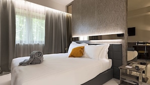 A modern hotel room with a large bed, a bedside table with a lamp, and a view of the outdoors through sheer curtains. - Albavilla Hotel & Co. (Albavilla)