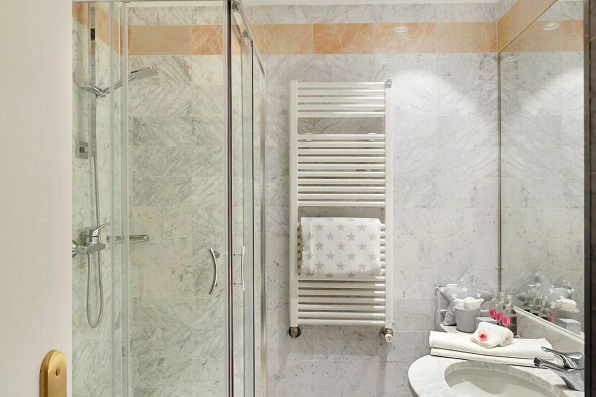 Un baño moderno con ducha envuelta en vidrio, un lavamanos blanco y un perchero con toallas estampadas.