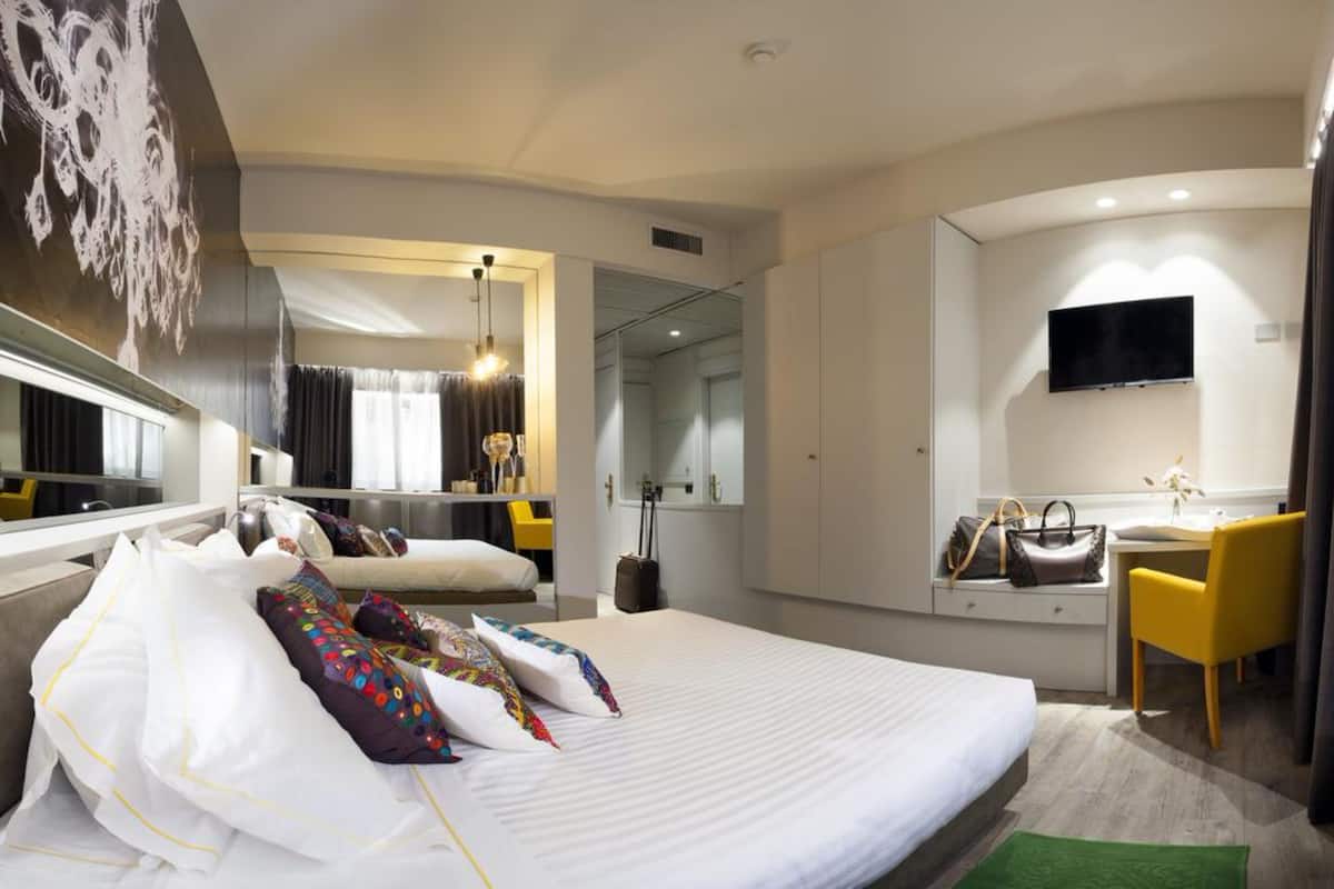 Una habitación de hotel moderna con una cama grande, un escritorio, una silla, un televisor y un baño visible a través de una puerta abierta.