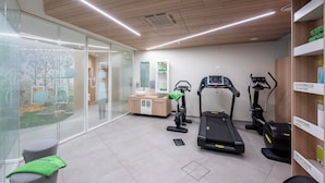 A modern fitness room with exercise equipment, a glass wall with a view, and a wooden ceiling. - Airport Hotel (Bagnatica)