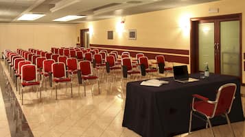 Un salón de conferencias con filas de sillas rojas, una mesa con una computadora portátil y una botella de agua.