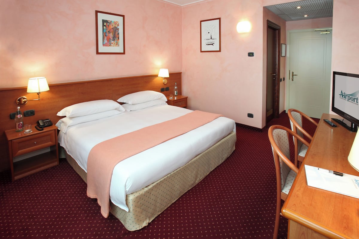 A hotel room with a bed, bedside lamps, a desk with a chair, and a television.