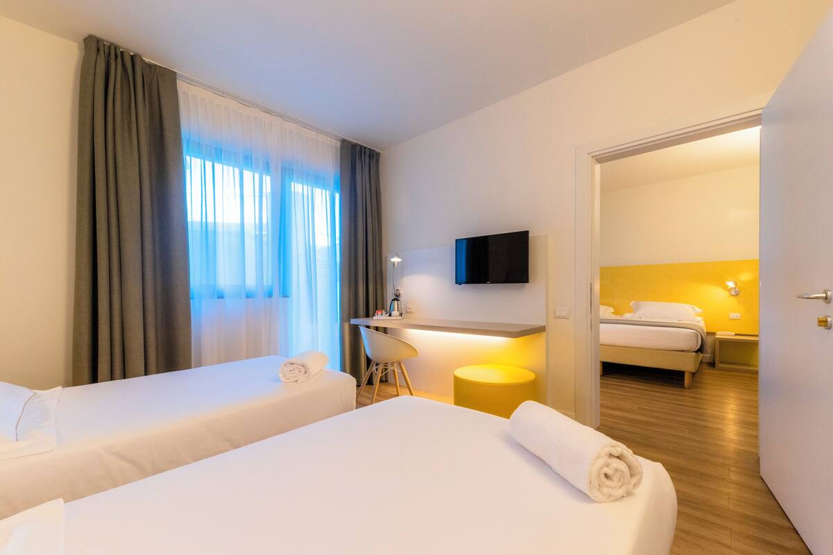 A hotel room with two beds, a desk, a chair, a TV, and a bathroom visible through an open door.