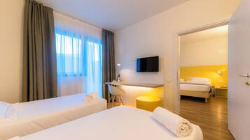 Habitación de hotel con dos camas, un escritorio, una silla, un televisor y un baño visible a través de una puerta abierta.