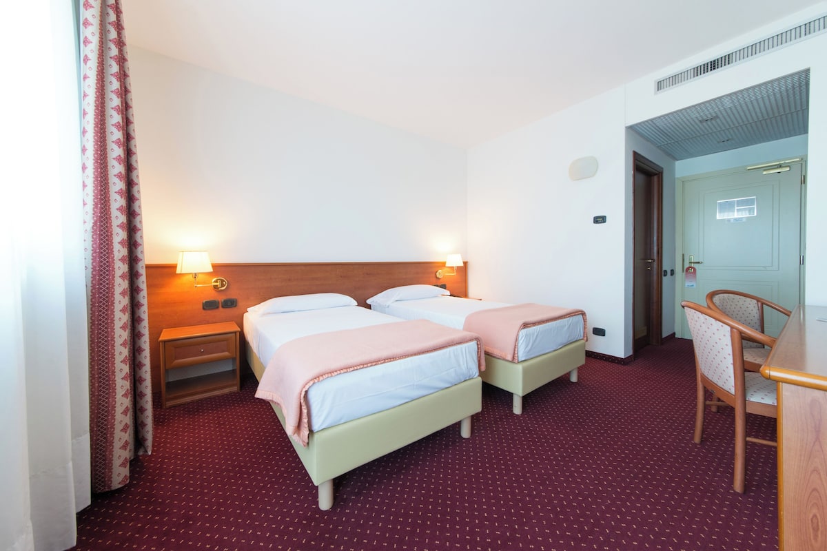 A hotel room with two beds, a desk, and a chair. There are two bedside tables with lamps.