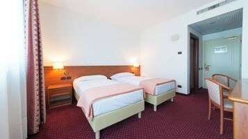 A hotel room with two beds, a desk, and a chair. There are two bedside tables with lamps.