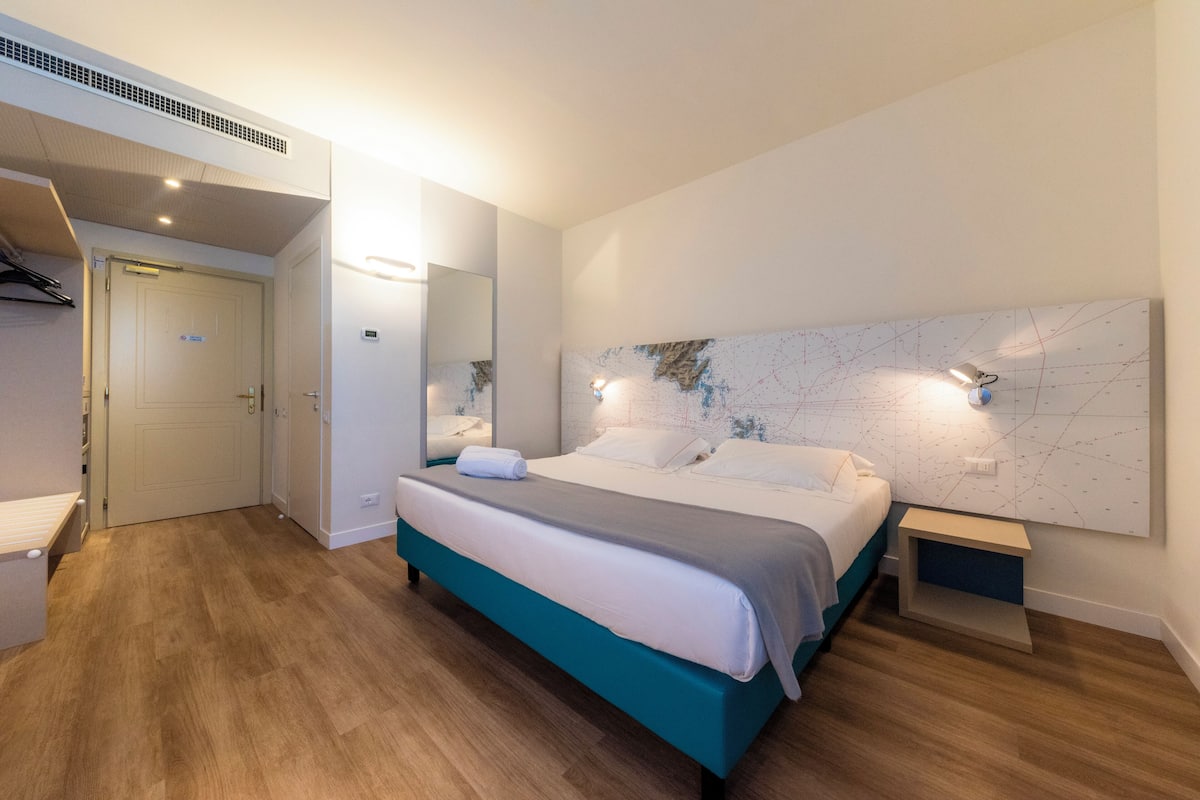 A modern bedroom with a bed, bedside tables, a mirror, and a map on the wall.