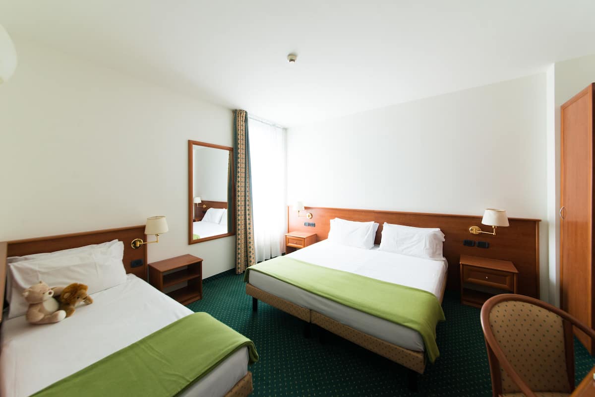 A hotel room with two beds, a chair, a nightstand, a lamp, and a mirror.
