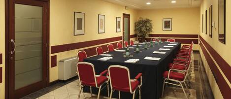 Un salón de conferencias con una larga mesa, sillas rojas y cuadros en las paredes.