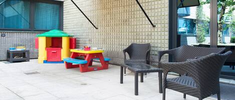 Un patio con sillas de mimbre, un área de juegos para niños y una mesa.