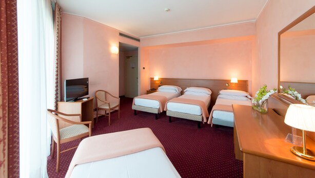 Une chambre d’hôtel avec deux lits simples, un bureau avec une lampe, une télévision et une chaise.