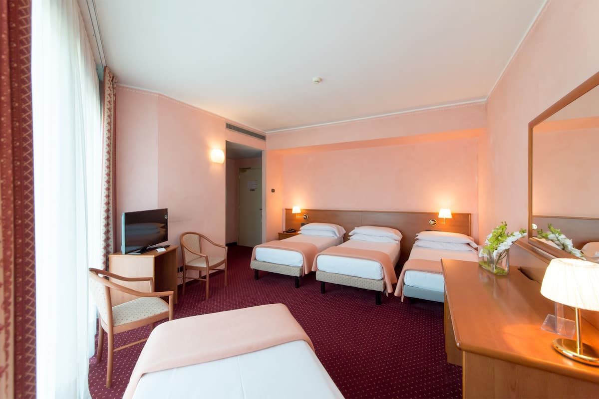 A hotel room with two single beds, a desk with a lamp, a TV, and a chair.